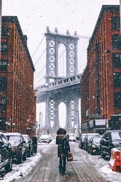 two people walking down a snowy street in front of the brooklyn bridge, with cars parked on both sides