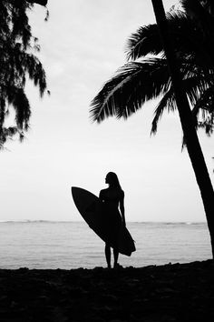 a woman holding a surfboard standing on top of a beach next to the ocean