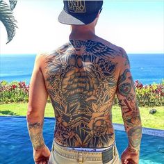 a man with tattoos on his back standing next to a pool and looking at the ocean