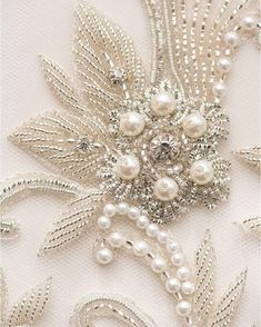 a close up view of a brooch with pearls and leaves on white fabric background