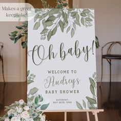 a welcome sign for a baby shower with greenery and flowers on it in front of a wooden easer