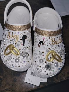 a pair of white and gold baby shoes with wedding rings on the bottom, sitting on a table