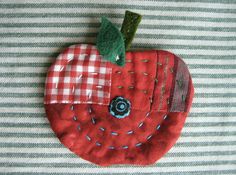 an apple made out of fabric on top of a striped cloth tablecloth with a green leaf sticking out of it