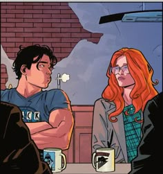 two people sitting at a table in front of a brick wall, one with red hair and glasses