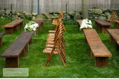 a long table set up with white chairs and greenery on the tables for an outdoor event