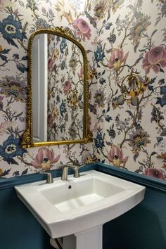 a white sink sitting under a mirror next to a wall papered with floral designs