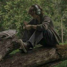 a woman sitting on top of a tree branch in the woods wearing headphones and listening to music