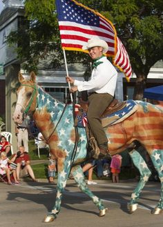 a man riding on the back of a horse with an american flag in his hand