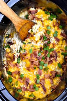 a wooden spoon in a crock pot filled with eggs and bacon, topped with green onions