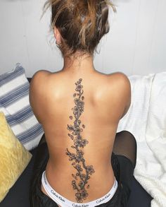 a woman with a back tattoo sitting on a bed