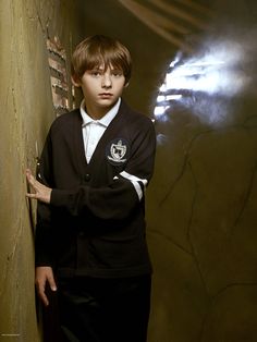 a young boy leaning against a wall with his hand on the corner and looking at the camera