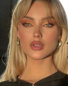 a woman with blonde hair and gold eyeshadow is posing for a photo in front of a mirror