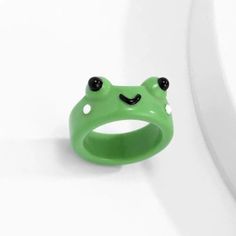 a green frog ring with black eyes on it's face, sitting on a white surface