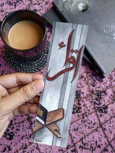 a person is holding a book with arabic writing on it next to a cup of coffee