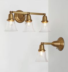 three light brass bathroom fixture with clear glass shades on the sides and an antique style arm