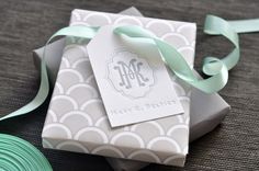 a white gift box with a green ribbon and monogrammed tag on it sitting on a table