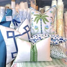 many pillows are stacked on top of each other in front of an assortment of fabrics