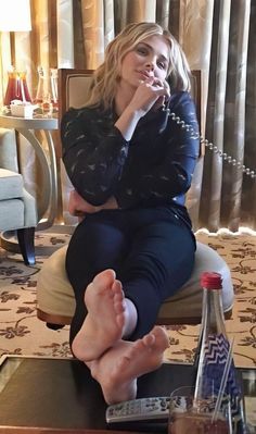 a woman sitting in a chair talking on the phone with her foot propped up next to a bottle of water