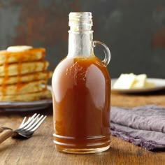 a glass bottle filled with syrup sitting on top of a wooden table next to pancakes