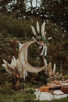 an outdoor table set up in the woods for a party with feathers and flowers on it