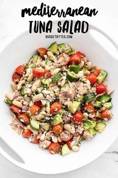 a white bowl filled with tuna and cucumber salad on top of a marble table