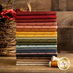 a stack of different colored fabrics sitting on top of a table next to a basket