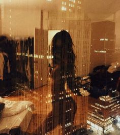 a woman standing in front of a window looking out at the city lights and skyscrapers