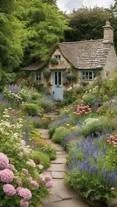 a garden with lots of flowers next to a house in the middle of trees and bushes