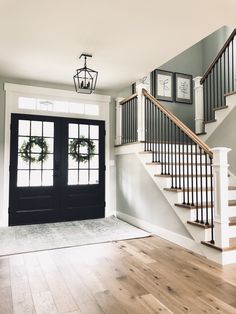 an empty entryway with stairs and wreaths on the door, next to a set of windows