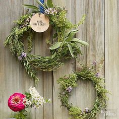 two wreaths made out of branches and flowers are hanging on a wooden fence,