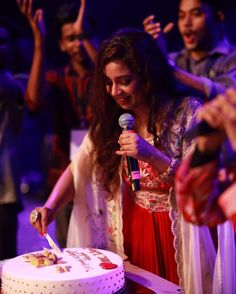 a woman standing in front of a cake holding a microphone