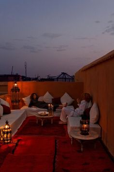 two people sitting on couches with candles lit up in front of them at night