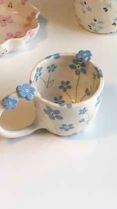 three bowls and two spoons with blue flowers on them sitting next to each other