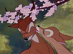 two deer standing next to each other under a tree with pink flowers on its head