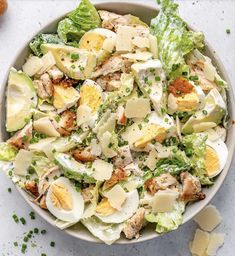 a salad with hard boiled eggs and lettuce in a bowl on a white surface