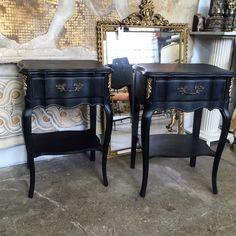 two black nightstands with gold trim on them in front of a mirror and wall