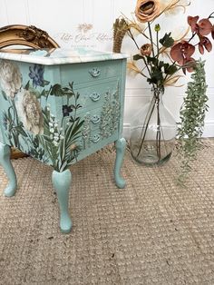 an old dresser with flowers painted on it and some vases full of flowers next to it