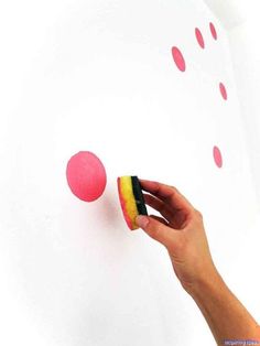 a hand holding a sponge next to a pink and yellow ball on a white wall