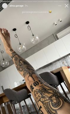 a man with tattoos on his legs and arms sitting in front of a kitchen counter