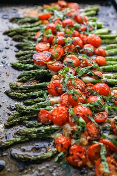 asparagus, tomatoes and other vegetables are lined up on a baking sheet