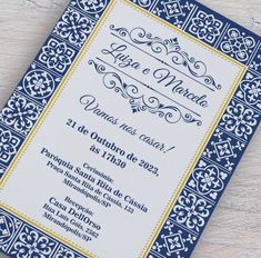 a blue and yellow wedding card with an ornate design on the front, sitting on top of a wooden table