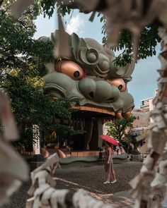 a woman holding an umbrella standing in front of a building with a dragon head on it