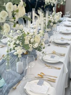 a long table is set with white flowers and gold place settings for an elegant dinner