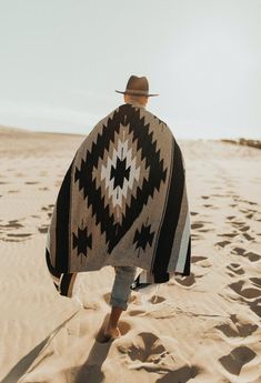 a person walking in the sand with a blanket over their shoulders and hat on his head