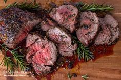 some meat is sitting on a cutting board with rosemary sprigs and seasoning