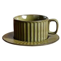 a green cup and saucer sitting on top of a metal plate next to each other