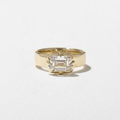 a yellow gold ring with an emerald cut diamond in the center on a white background