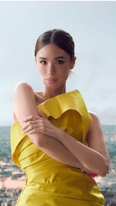 a woman in a yellow dress is posing for a photo with the city behind her