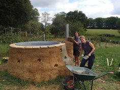 two people standing in front of a large round structure made out of hay and wood