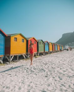 a woman in a red swimsuit walking on the beach next to colorful bathing huts